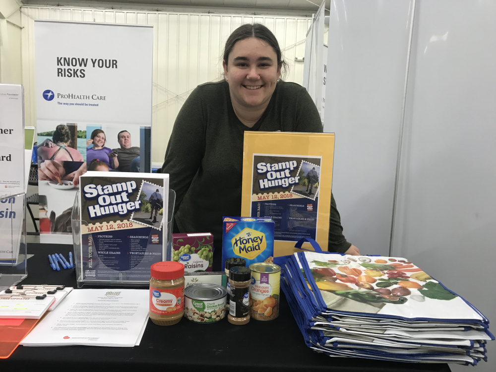Young girl, a Healthy Shelves intern, standing behind a table featuring posters, handouts and boxes and cans of healthy foods
