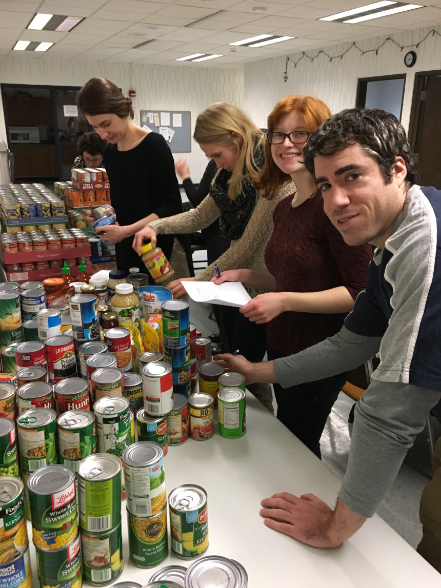 3 young women and a young man inventorying a table full of canned foods