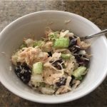 a white bowl with chunks of celery, red grapes and chicken plus shredded white cheese